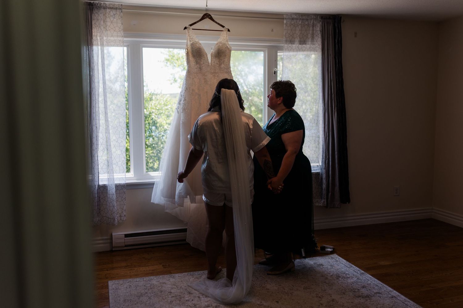 People carry white fabric while walking through an empty room with hardwood floors and green curtains by the windows.
