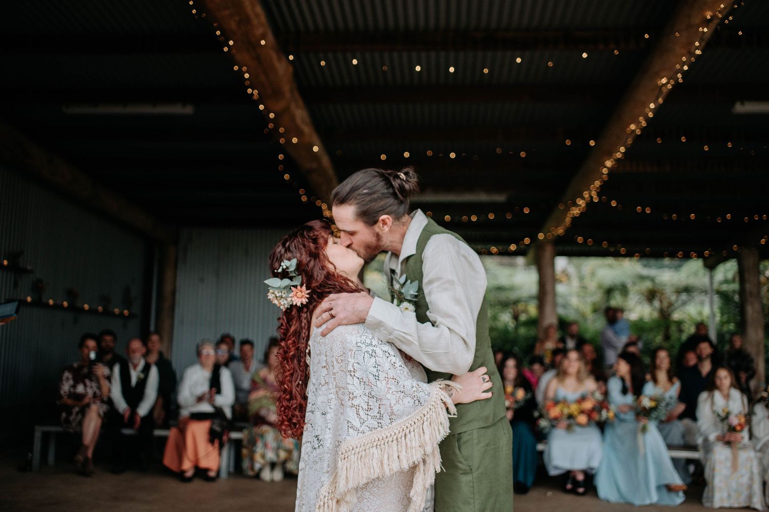 A couple shares a romantic moment while dancing together at an indoor wedding reception with twinkling lights.