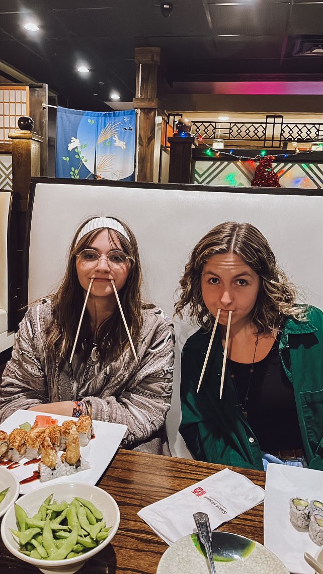 Friends enjoy Asian cuisine at a casual restaurant with sushi rolls and salad on wooden table.