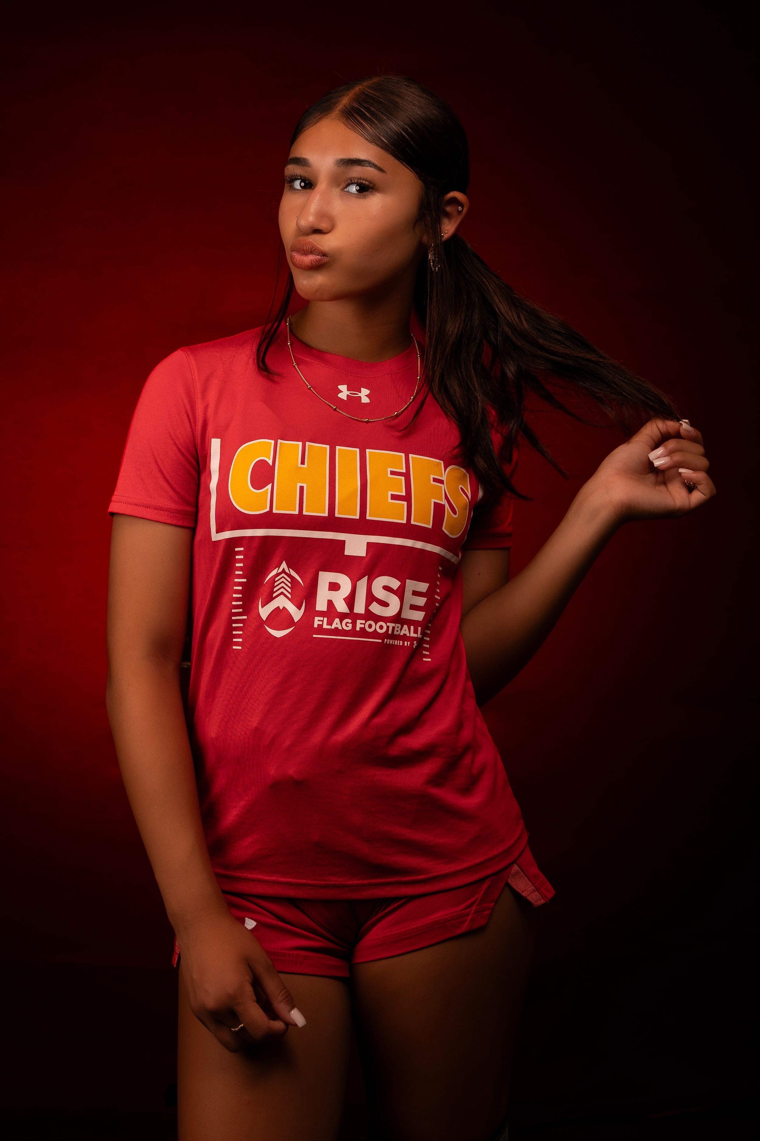 Athletic model wearing red Chiefs team uniform photographed in dramatic studio lighting.
