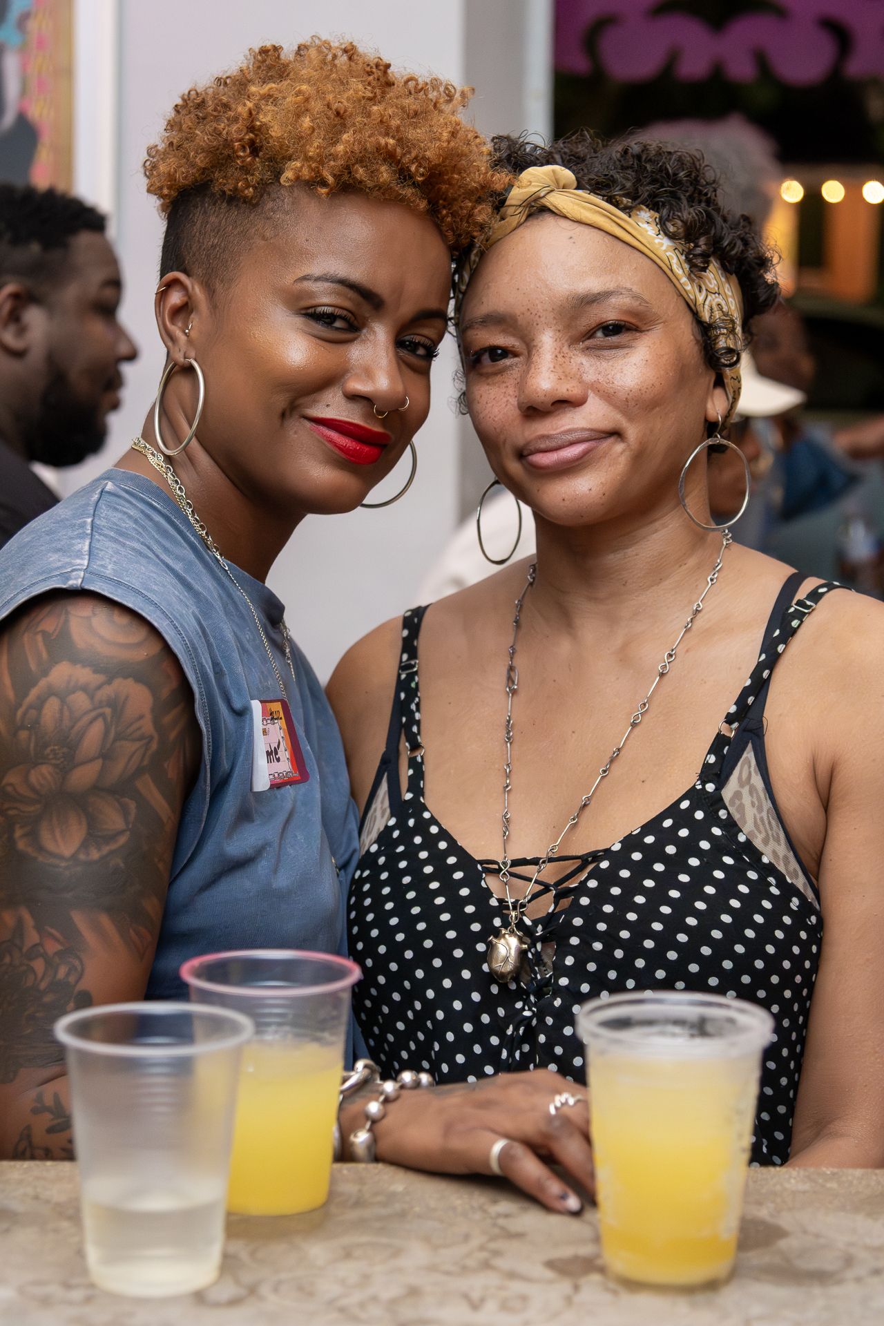 A romantic couple shares tender moments over drinks at a cafe table, wearing polka dots and hoop earrings.