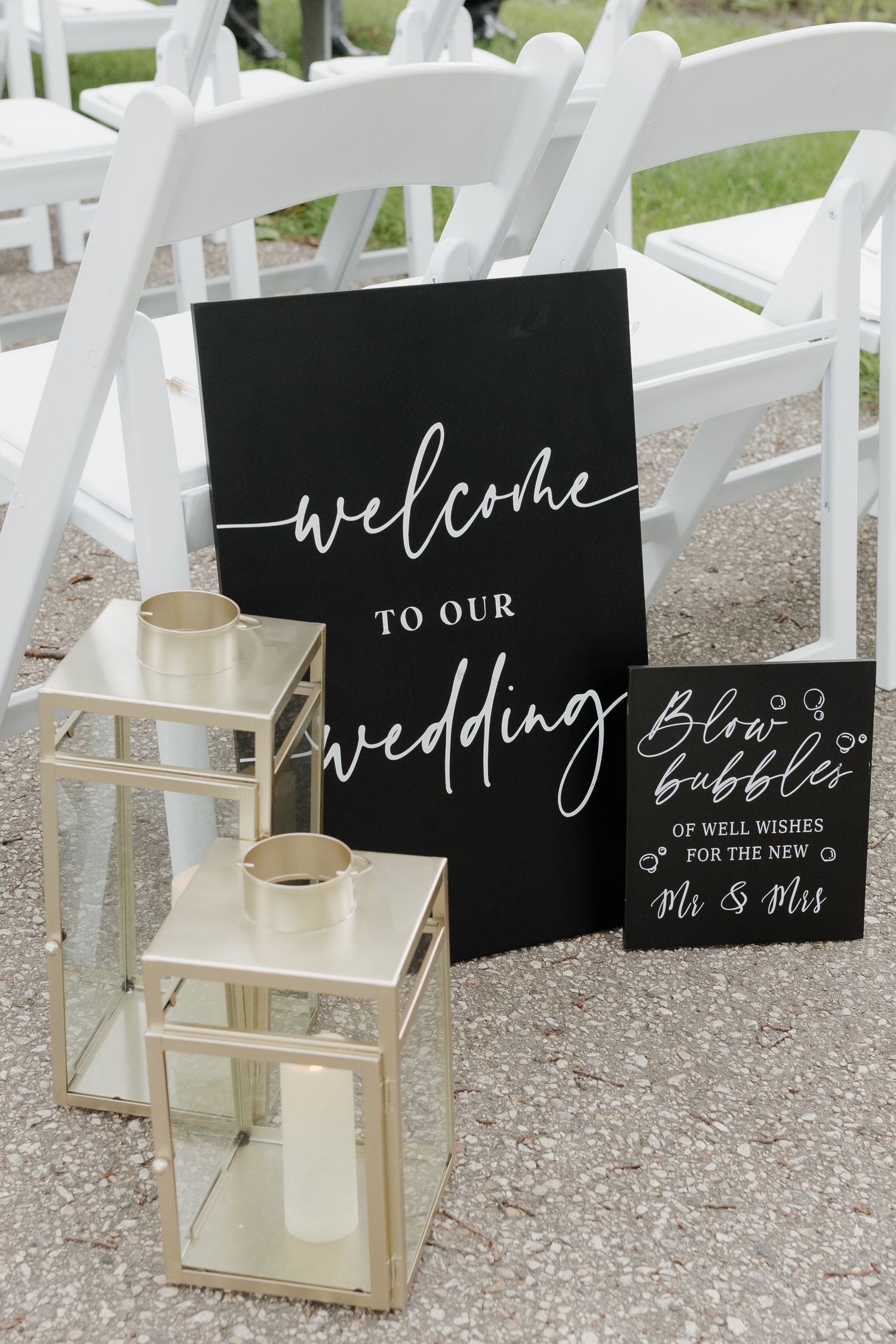 Black welcome signs with white calligraphy text and gold lanterns set up for an outdoor wedding ceremony.
