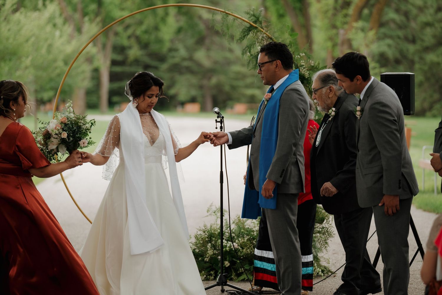Two people share a joyful first kiss during an outdoor wedding ceremony surrounded by trees and guests.