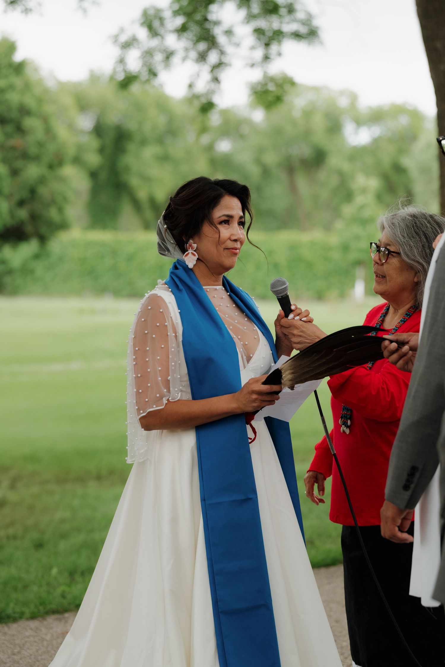 Wedding celebration with attendees gathered outdoors beneath shady trees.