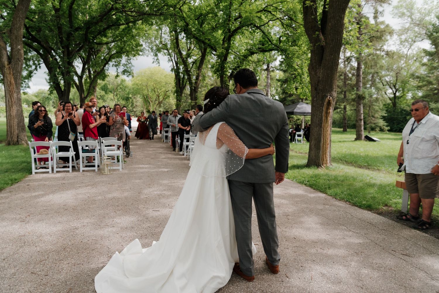 Wedding party processes down tree-lined path after outdoor ceremony.