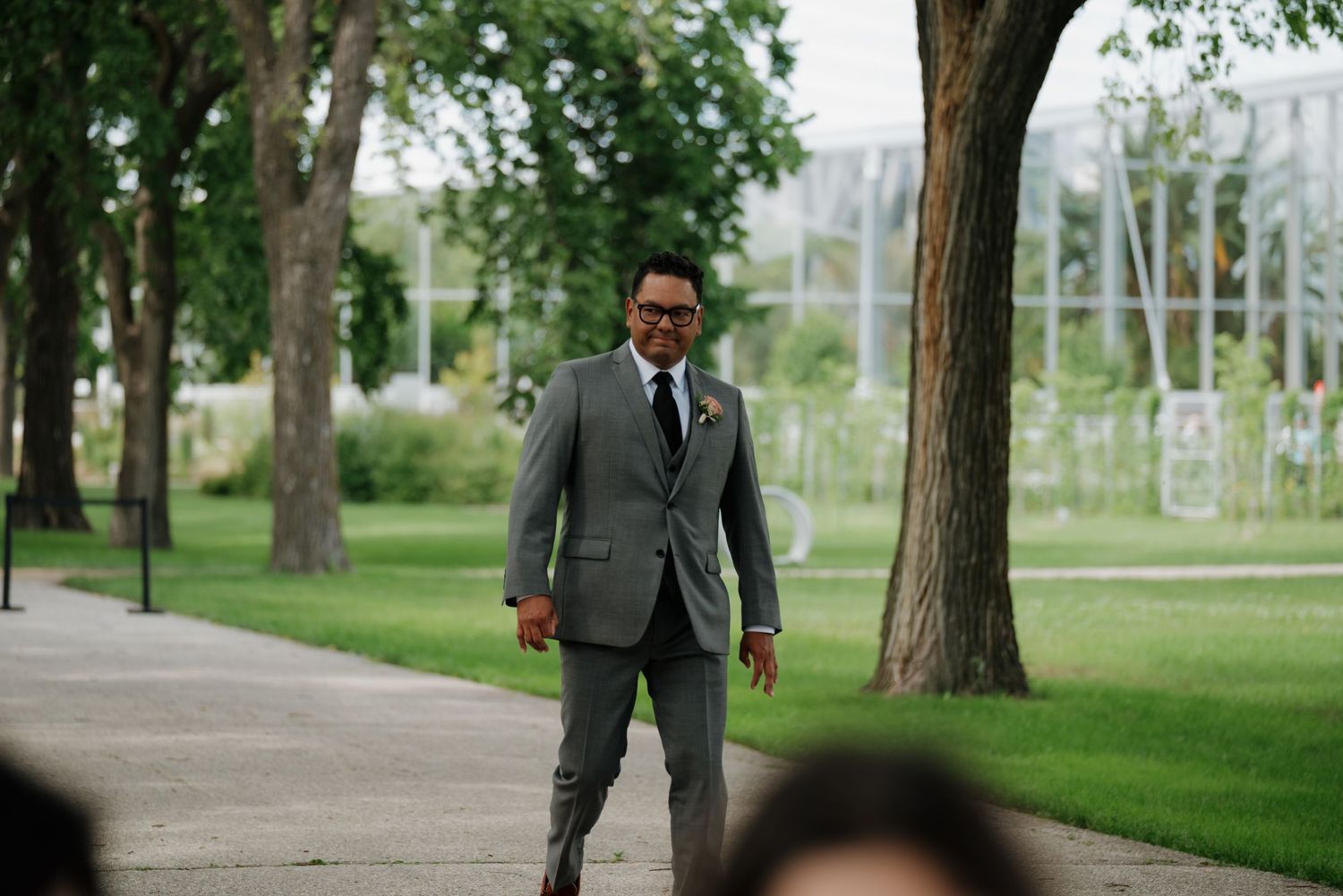 Wedding couple walks through a scenic summer park with tall trees and lush green grass creating a romantic atmosphere.