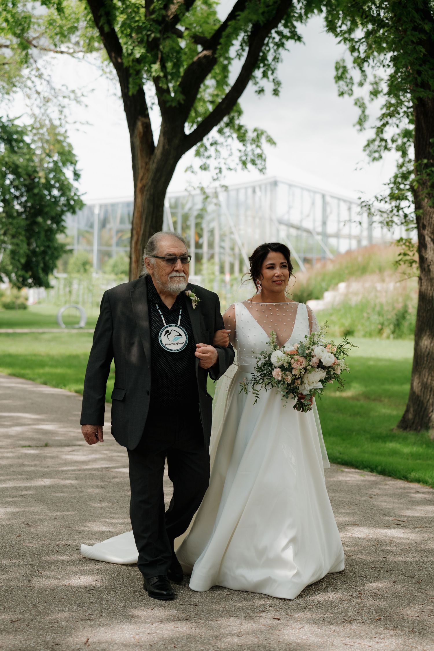 Wedding ceremony taking place on a tree-lined path in a park setting.