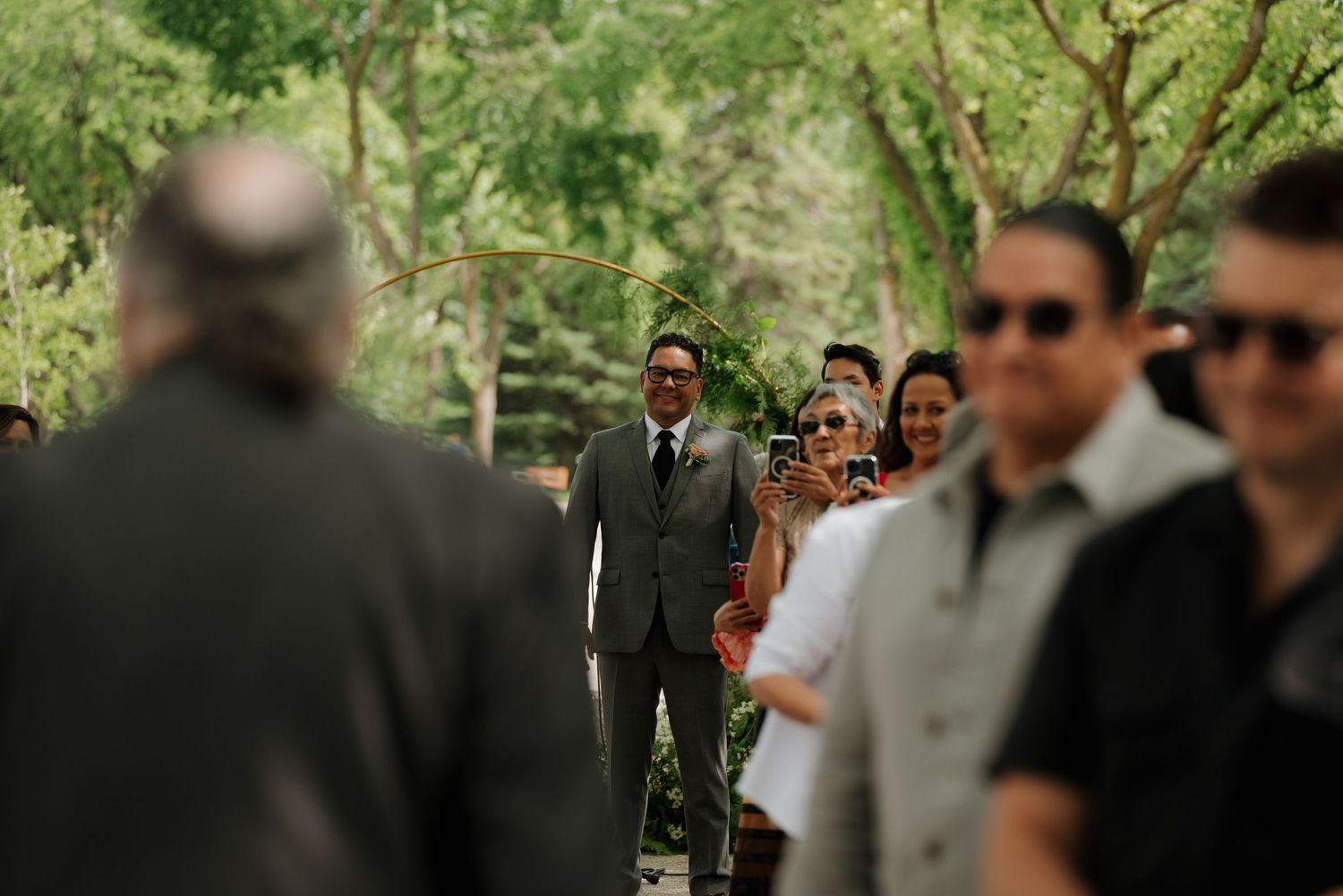 Outdoor wedding ceremony under green trees with guests gathered for the celebration.
