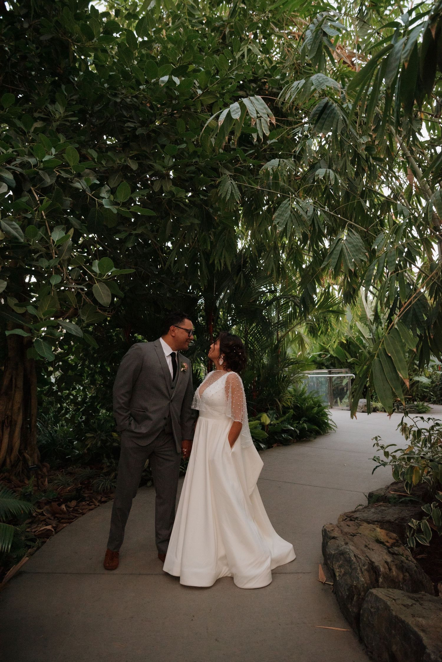 A wedding couple shares an intimate moment on a stone-lined path surrounded by tropical plants.