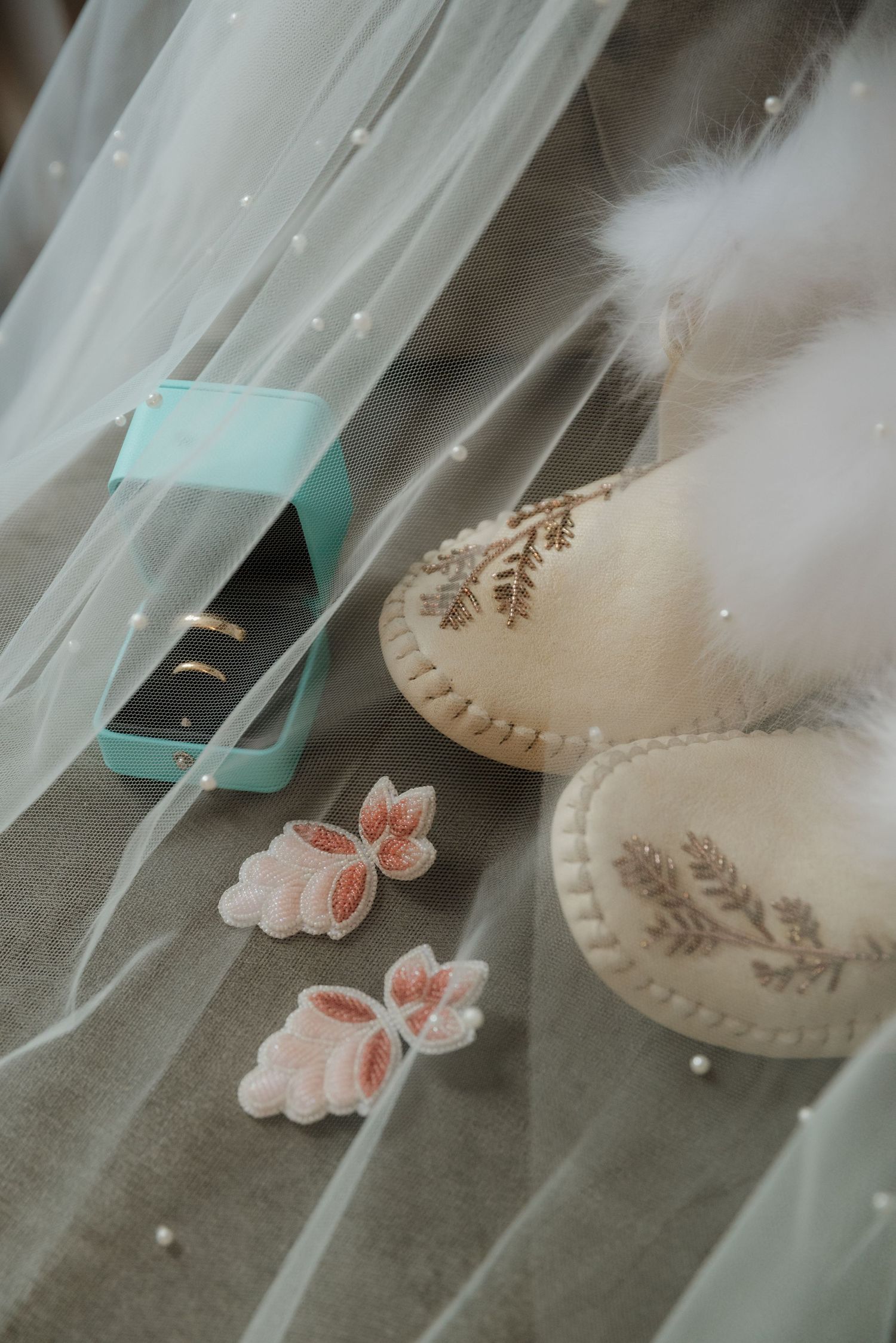 Bridal accessories with teal box, floral earrings, and fur-trimmed moccasins against white tulle.