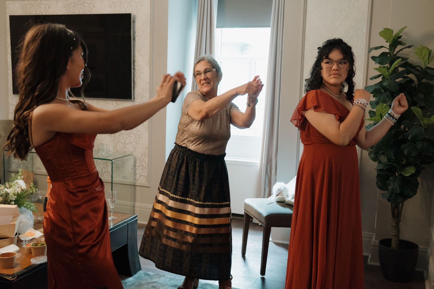 Three women in colorful dresses dancing together during a celebration in a brightly lit room.