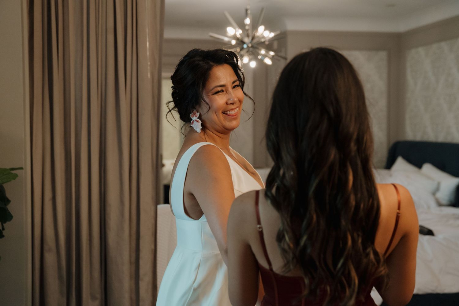 Two people sharing a joyful moment in an elegantly decorated bedroom with a modern chandelier.
