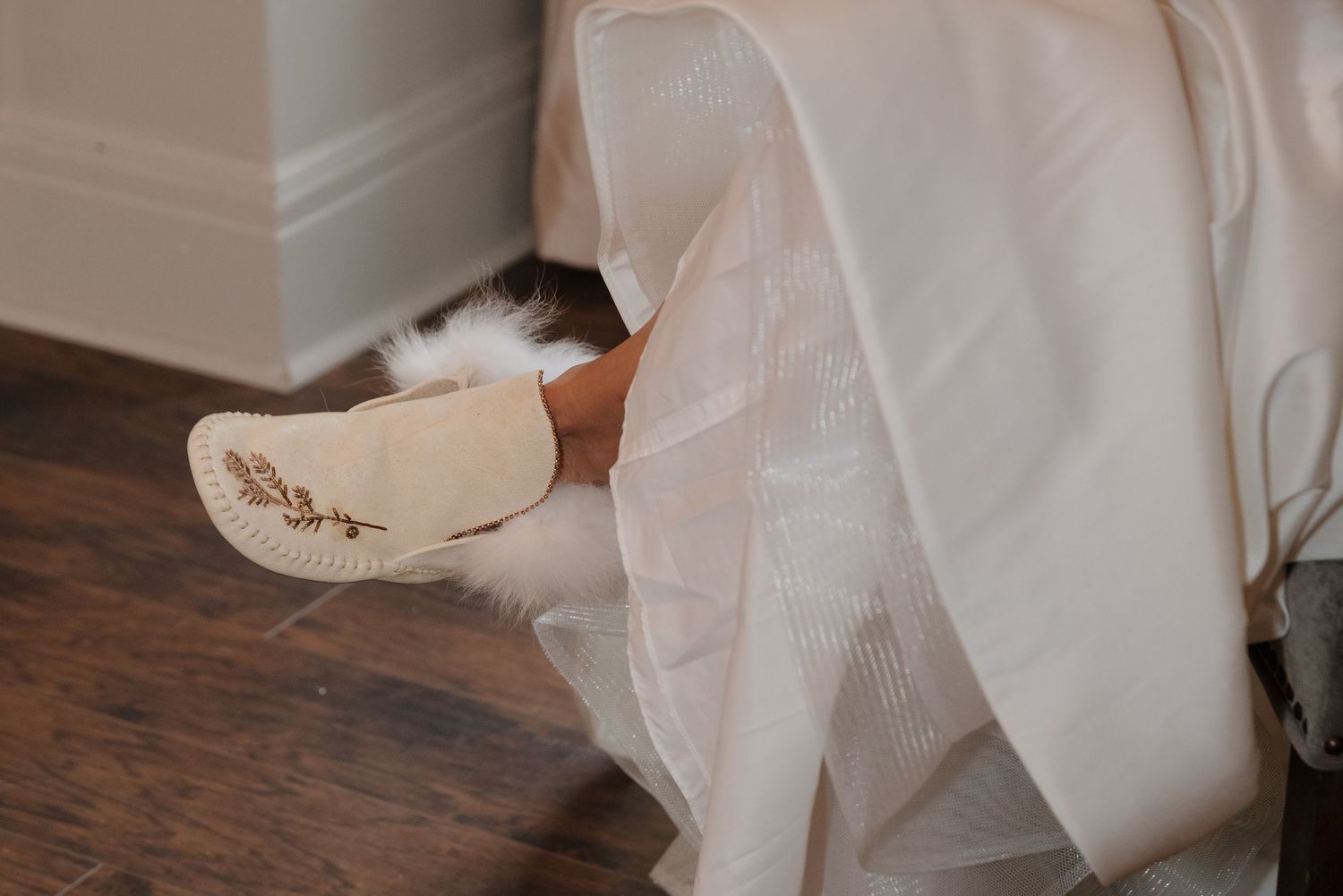 Close up detail of a white wedding dress skirt with textured fabric flowing across wooden flooring.