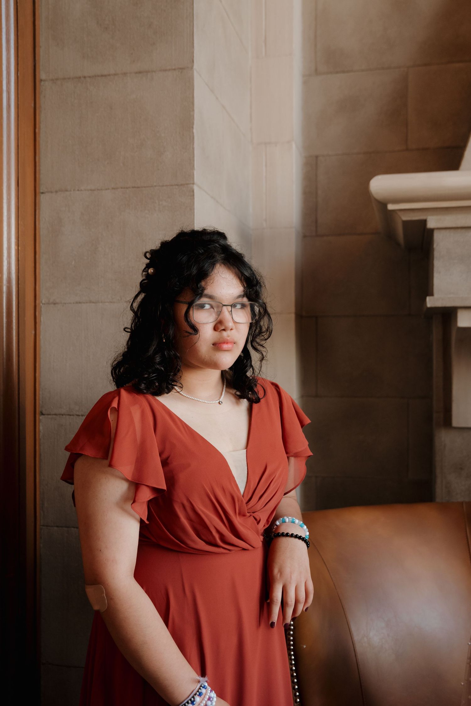 Person wearing red flutter sleeve dress and glasses seated in elegant interior.