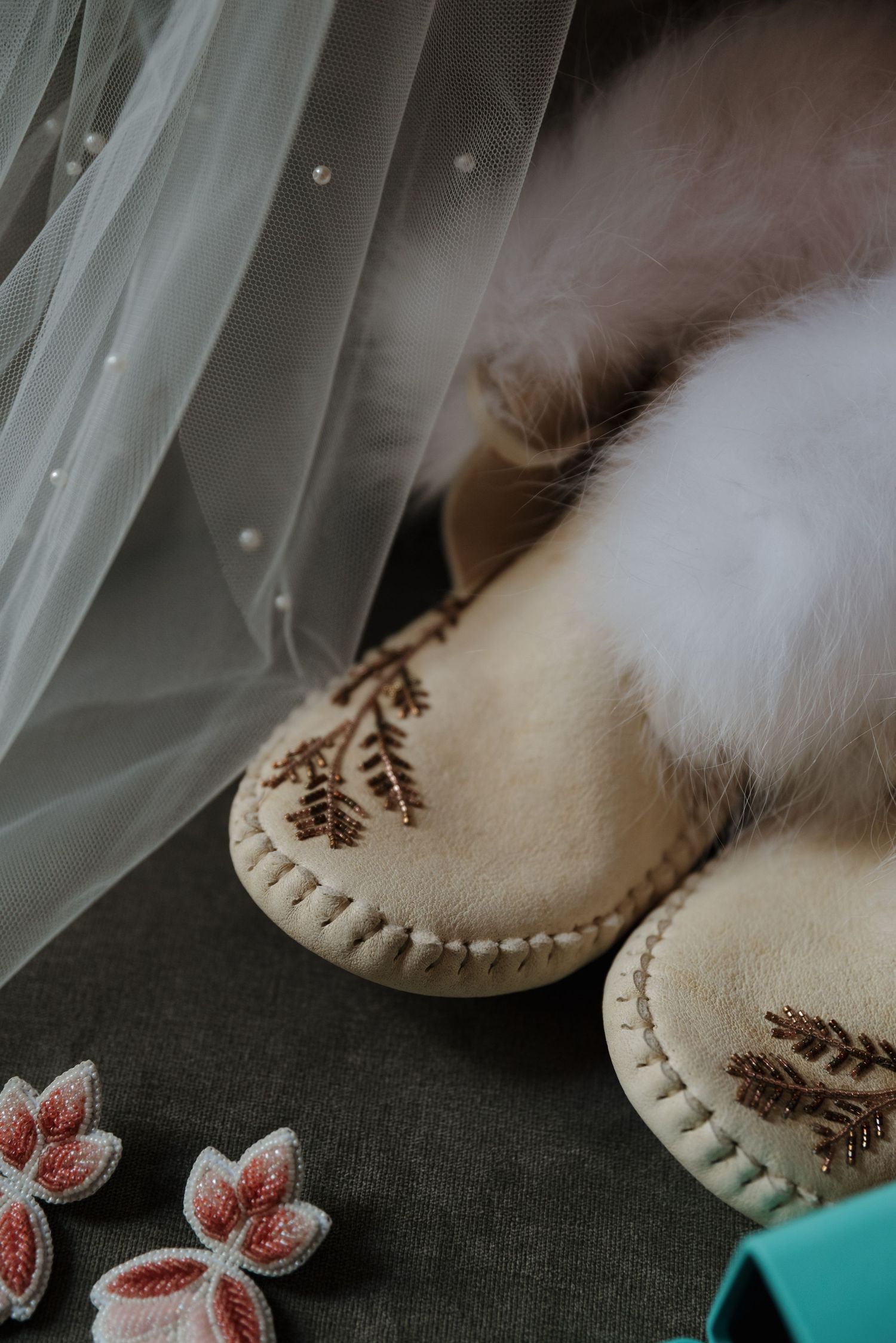 Decorative beaded moccasins with floral embroidery next to delicate fabric and pink flower accessories.