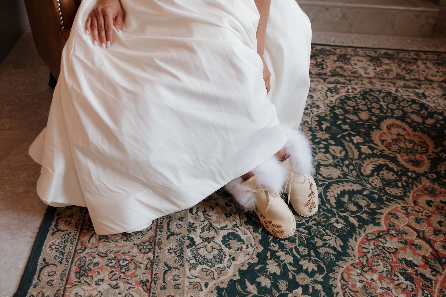 A formal white wedding dress draped across an ornate patterned vintage rug.