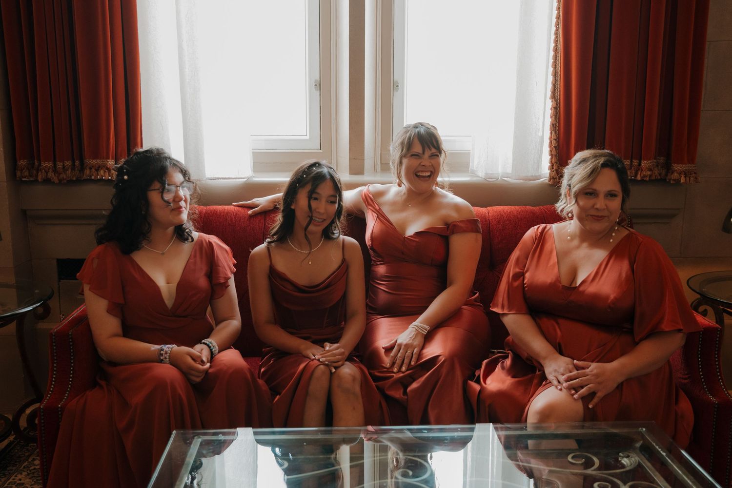 Four people in matching red dresses sit together on a couch by a window.