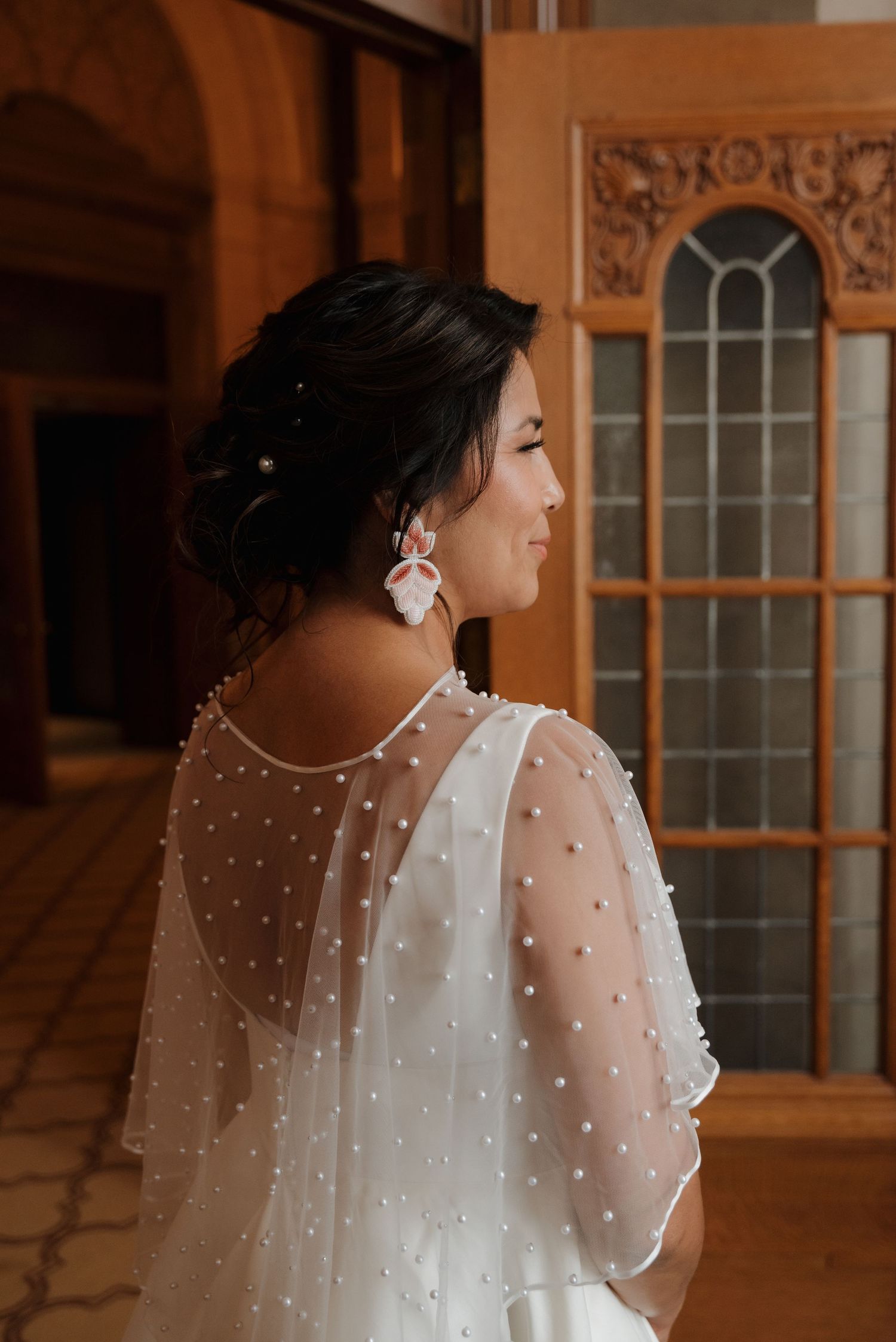 A delicate sheer polka dot wedding cape with pearl details drapes elegantly over a bridal gown.