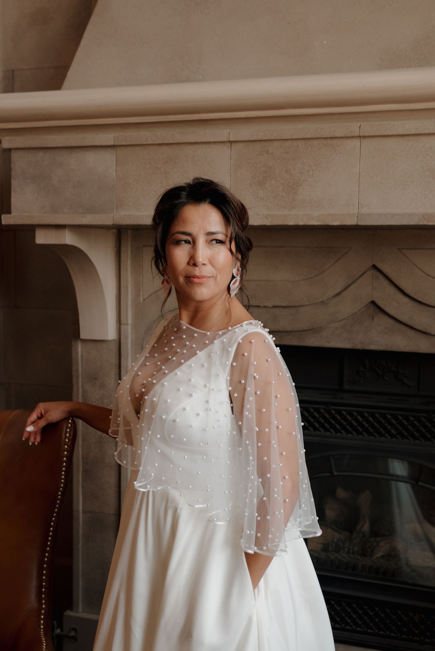 Close-up details of an elegant white lace wedding dress with sheer sleeves captured in soft indoor lighting.