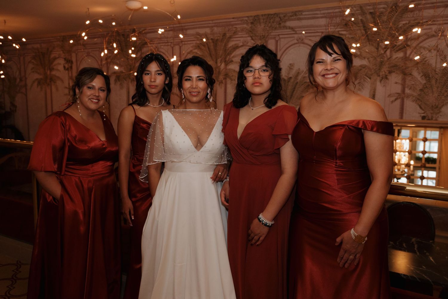 Wedding party in burgundy dresses posing together with twinkling lights.