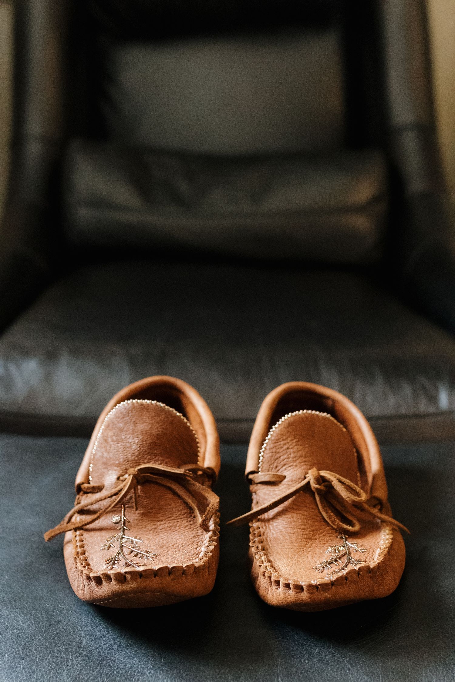 A pair of brown leather moccasin shoes displayed on a black leather chair.