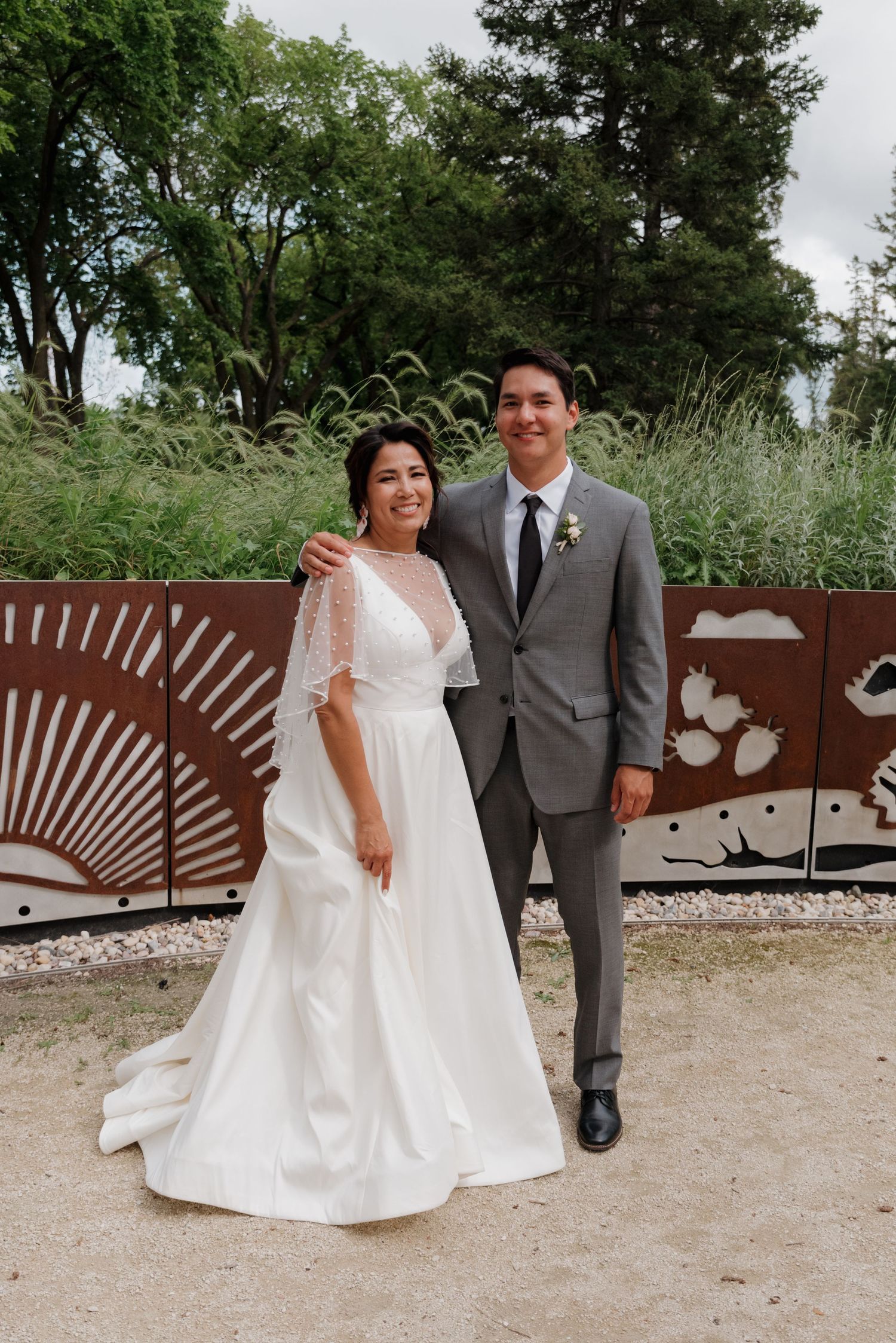 Wedding couple poses in front of decorative metal art installation outdoors.