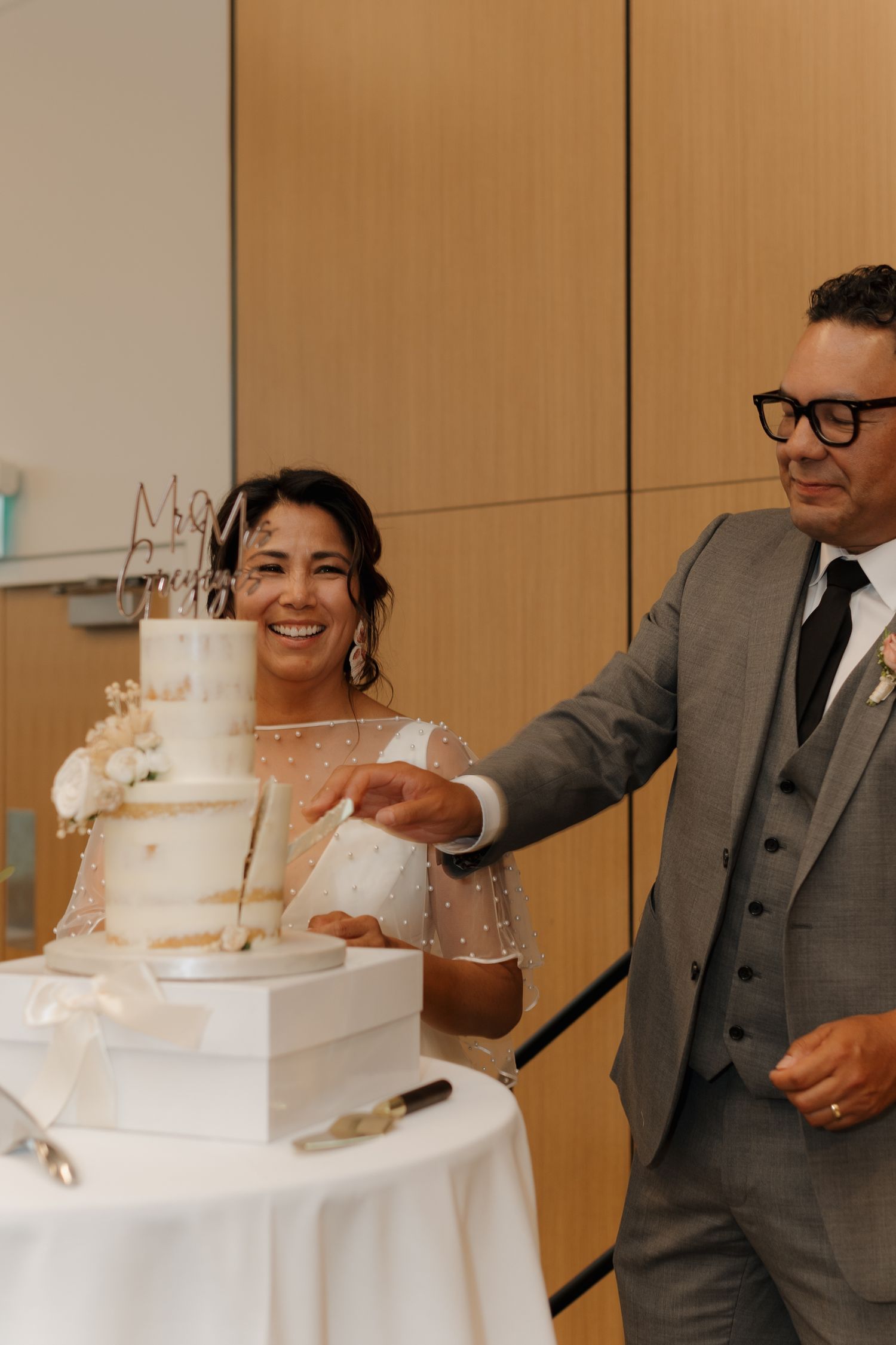 A tiered white wedding cake is displayed as a couple prepares to cut it during their reception.