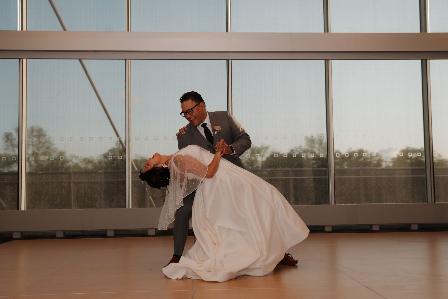 Wedding couple dancing together in a modern venue with floor to ceiling windows.
