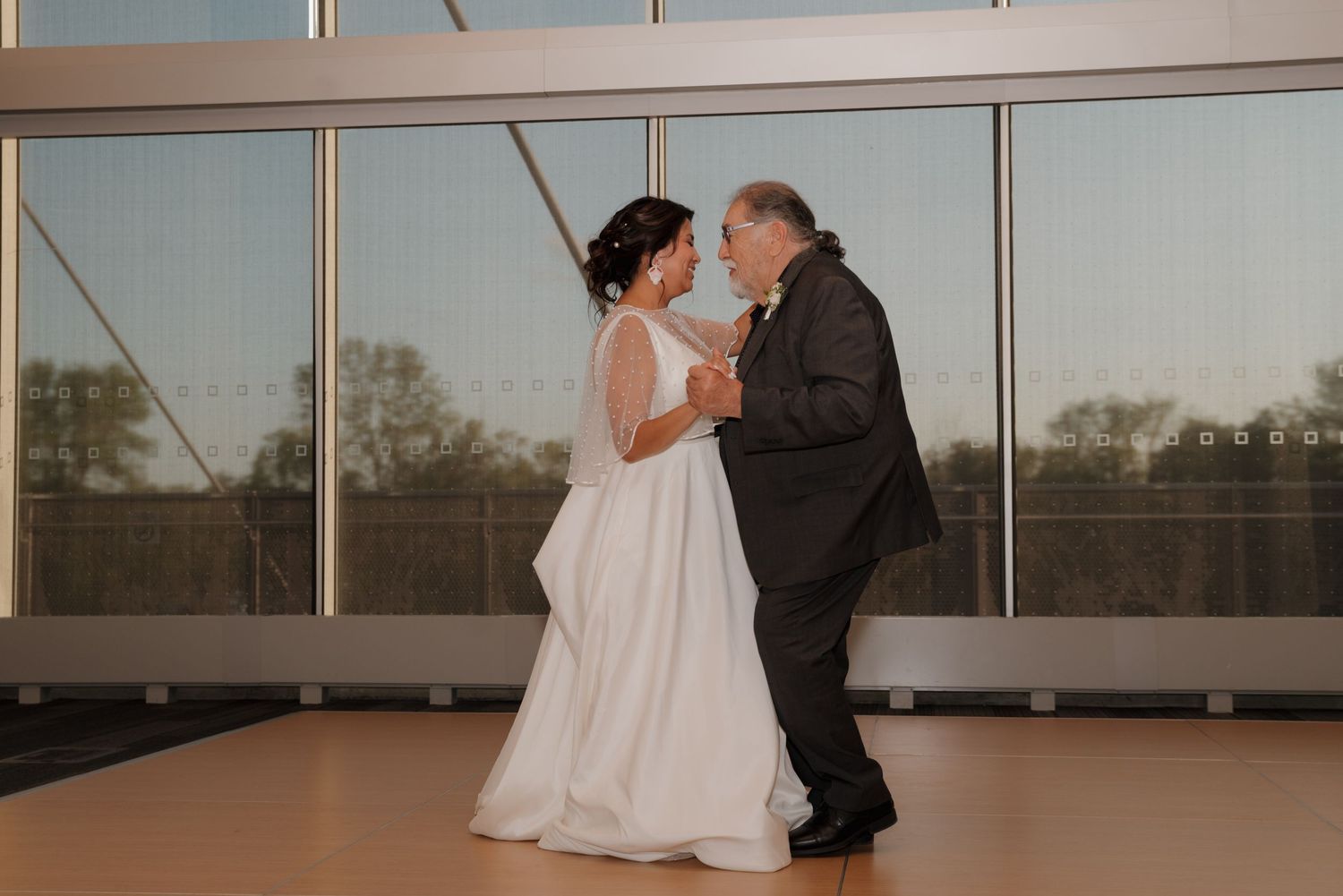 A couple enjoys a romantic dance in front of large windows during their wedding celebration.