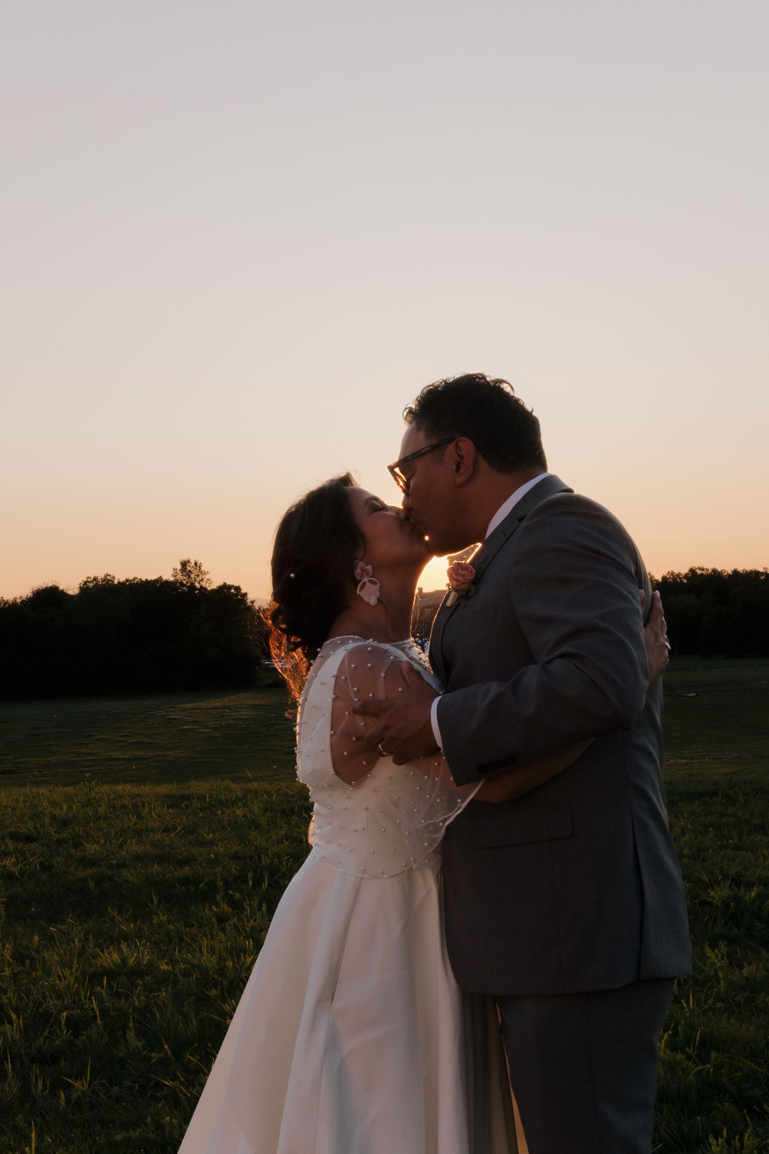 Romantic sunset silhouettes of newlyweds embracing in an open field during golden hour.