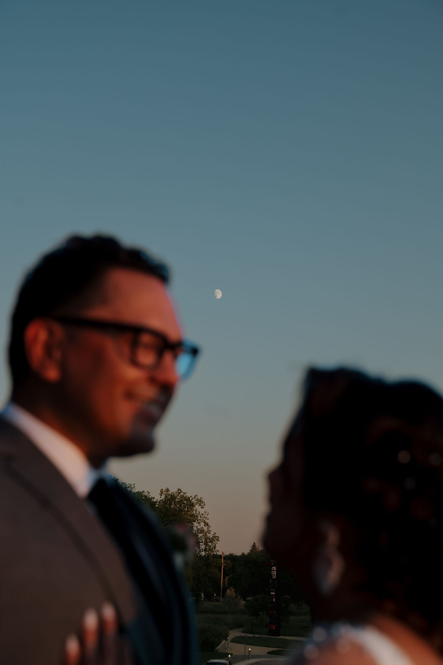 Artistic portrait of a couple against twilight sky with visible crescent moon.