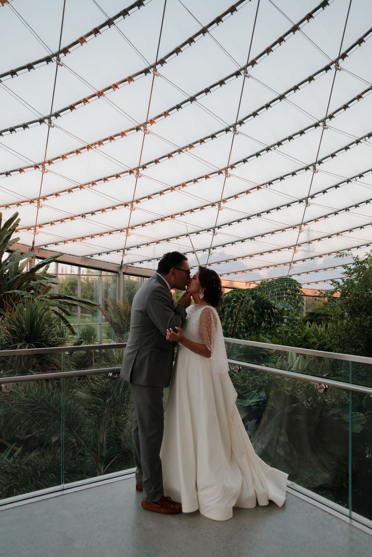 Wedding couple embracing under string lights on outdoor terrace.