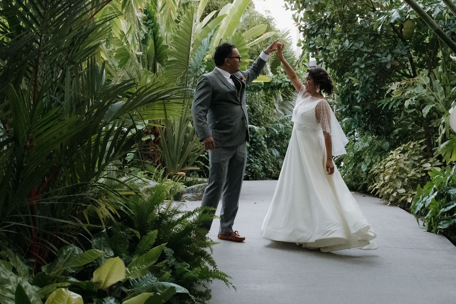 Newlyweds sharing intimate moments while walking through a lush tropical garden setting.