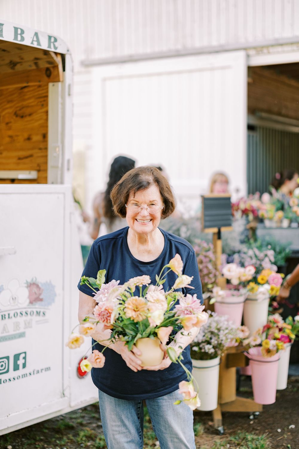 Woman in navy blue clothing joyfully examines fresh flower arrangements at an outdoor flower stand.