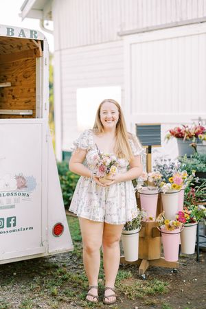 Young person wearing floral print clothing selects flowers from a rustic flower stand.