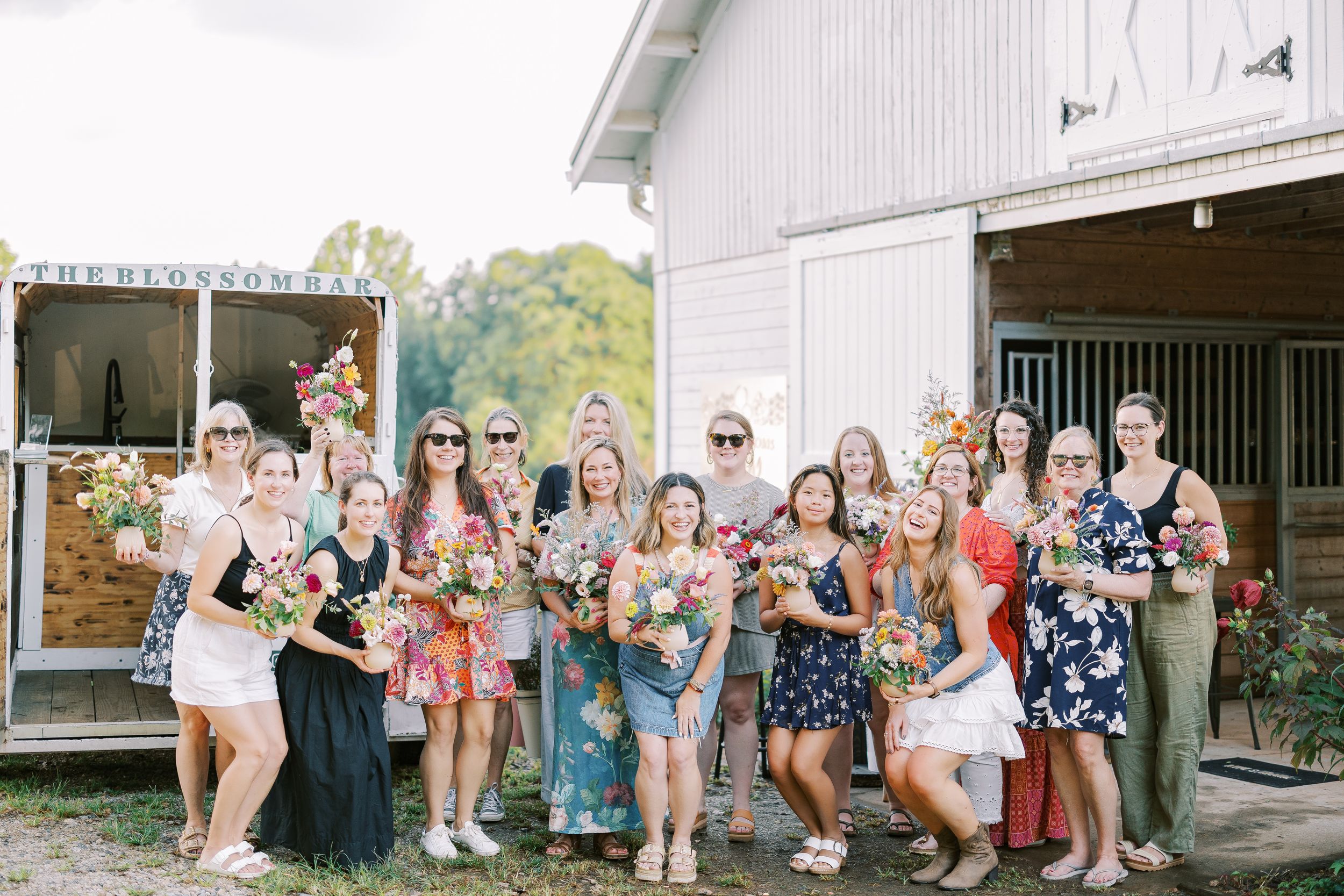 A cheerful group poses together in front of a rustic white barn on a sunny day.