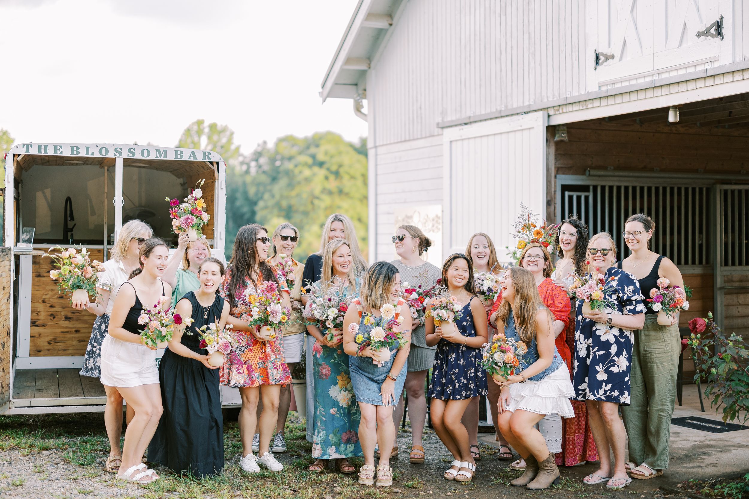A group of wedding guests stand in a line extending off-camera in a rustic outdoor setting for a photo opportunity.