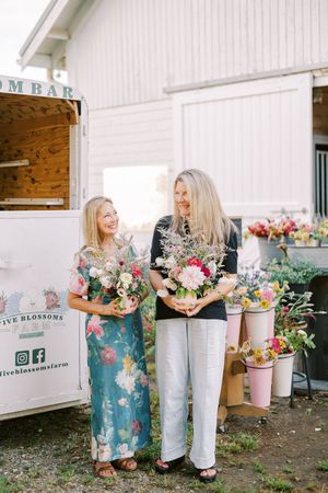 Two people holding colorful flower arrangements standing by a mobile flower bar outdoors.