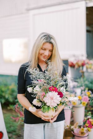 Vibrant floral bouquet being held in front of a white barn with mixed flowers and greenery.