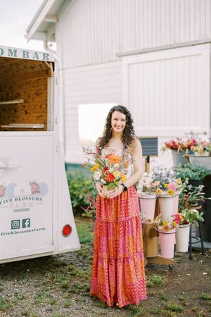 Person in long patterned dress holding colorful summer bouquet by mobile flower shop.