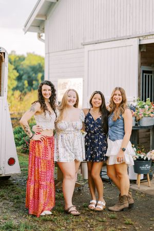 A group enjoys a sunny day outside a white barn with vintage decor and floral displays.