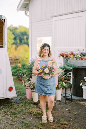 Person in denim dress holding fresh floral arrangement next to mobile flower shop.