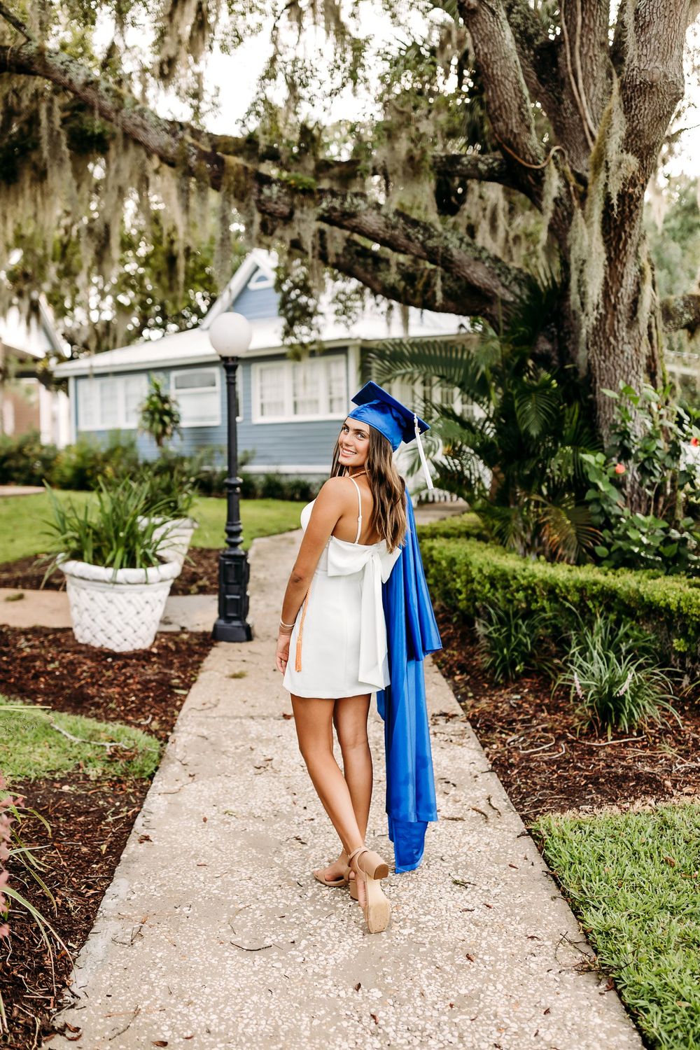 Someone in a white sundress and blue blanket walks along a garden path with Spanish moss draped trees overhead.