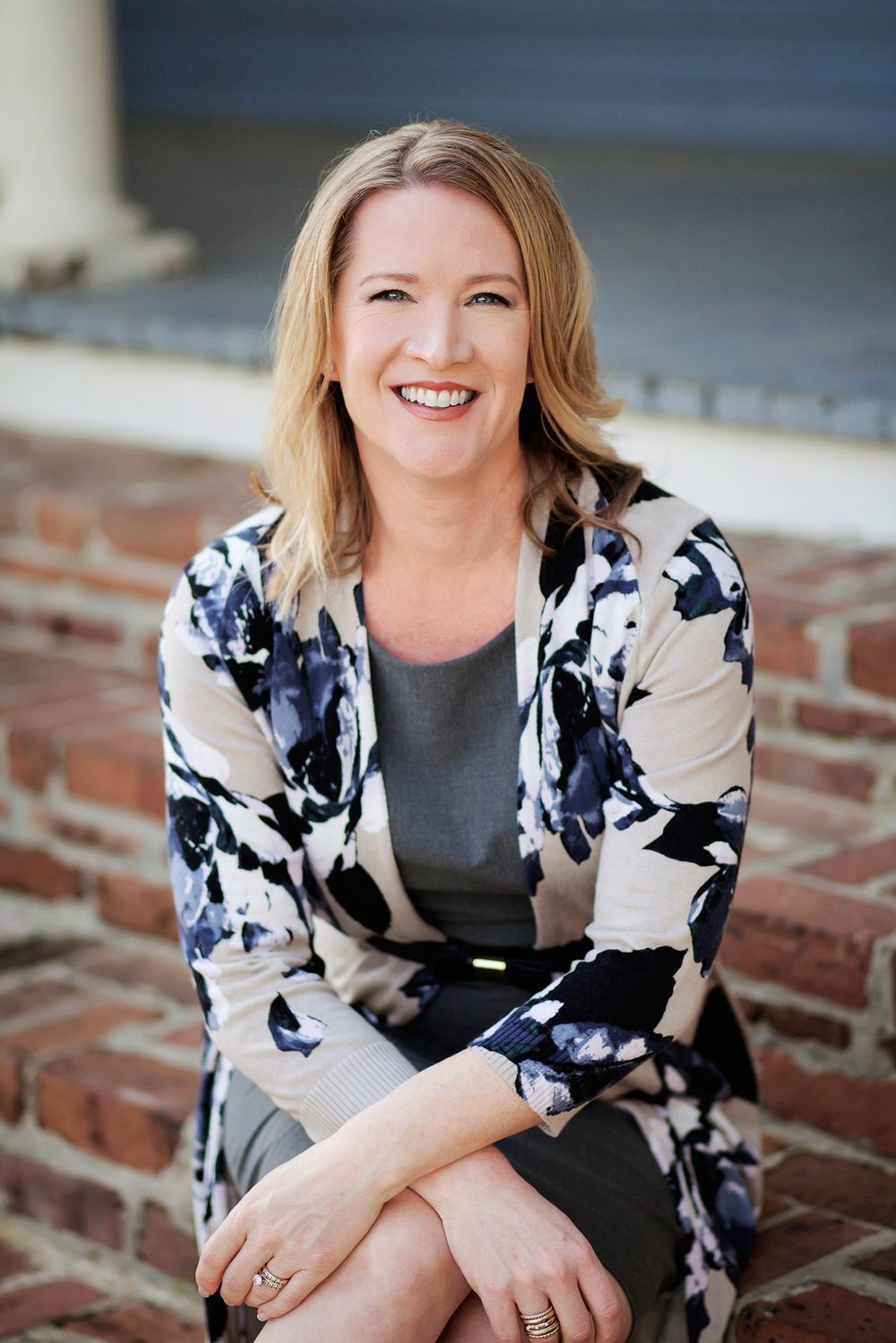 Professional headshot series showing confident person in black and white floral blazer sitting on brick steps outdoors.