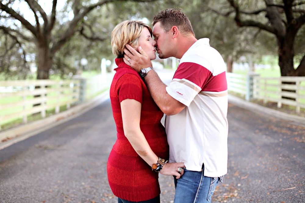 A couple in red and white clothing share an intimate moment on a tree-lined country road.