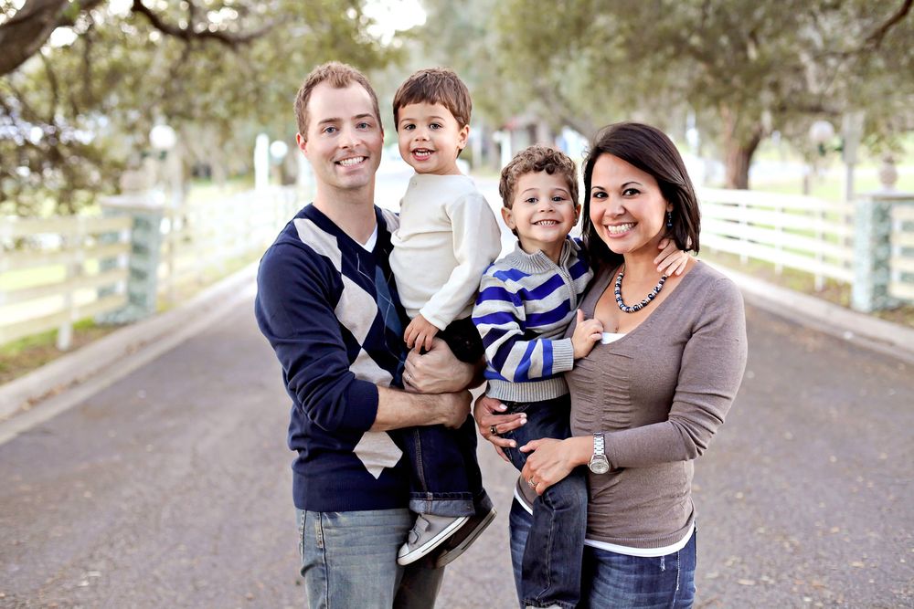 A happy family embraces outdoors in casual attire against a serene natural backdrop on a bright day.