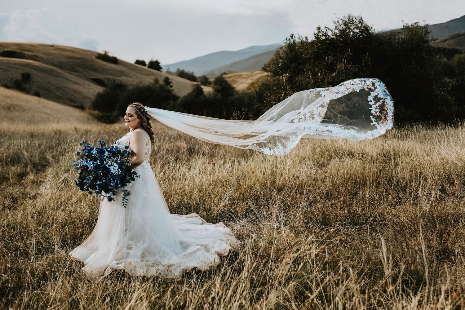 Blonde bride with curly hair and a braid wearing a cathedral veil in a Corinth, Texas field at sunset.