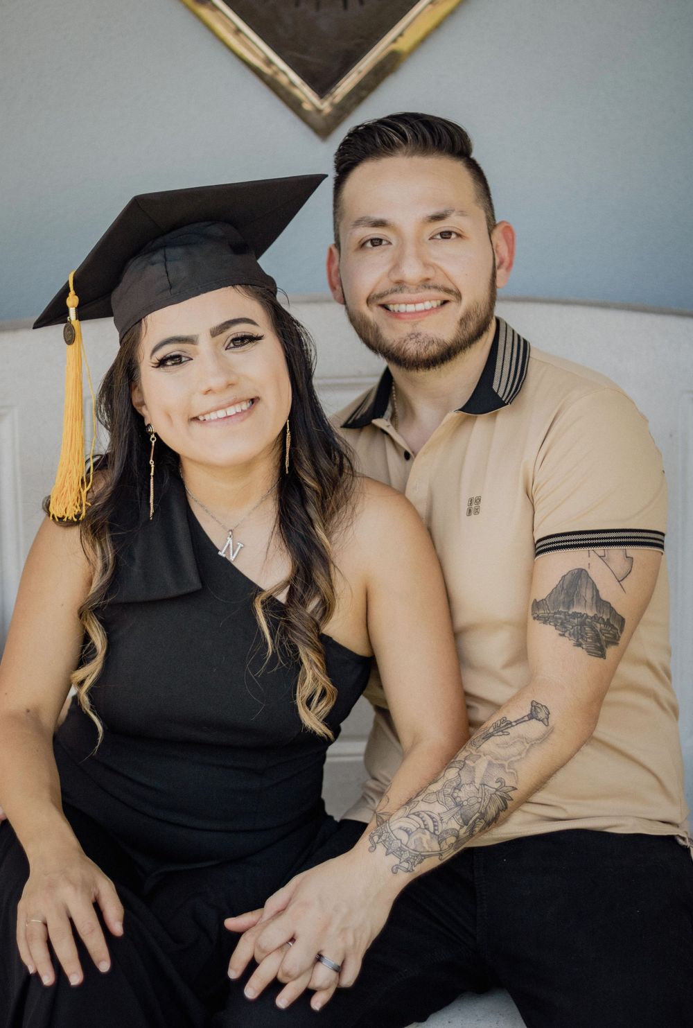 Couple posing together for graduation photos, woman wearing black cap and gown with gold tassel.