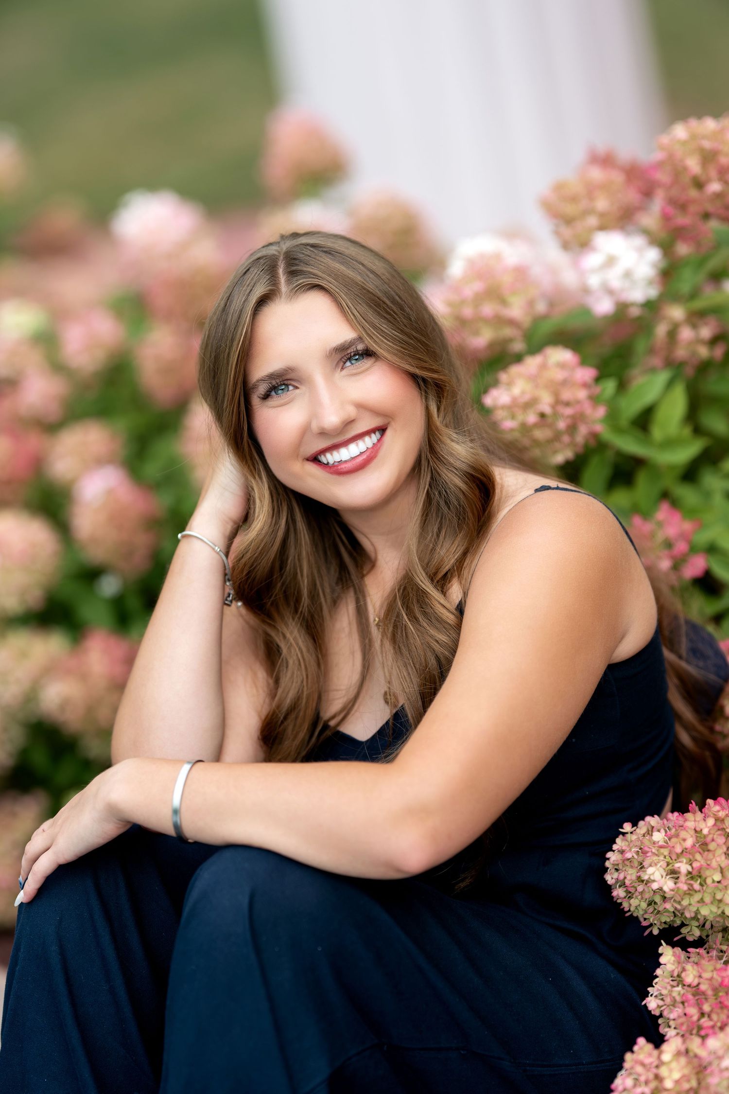 Smiling young woman with curly hair sits on bench surrounded by colorful tulips in garden.