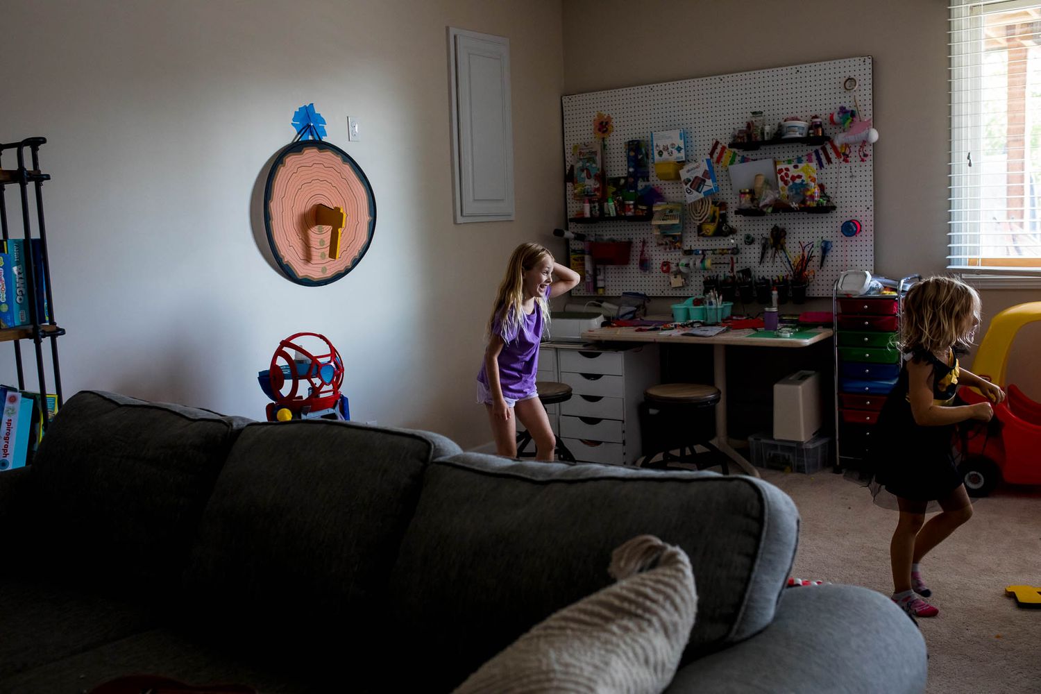 A child plays in a dimly lit living room with toys and storage shelves visible in the background.